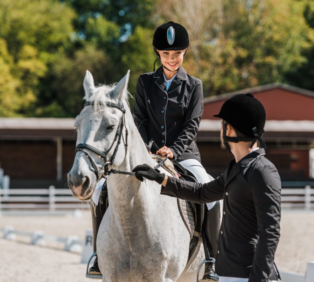 male equestrians holding horse halter female jockey sitting on horse at horse club.jpg